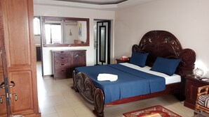 A bedroom with a wooden bed, a nightstand, a dresser, and a mirror. - Residence Hotel Kakatar (Dakar)