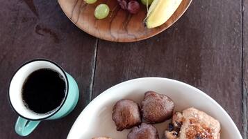 A wooden table with a bowl of mixed grapes and a banana, a mug of black coffee, and a plate with pastries and a grilled item.