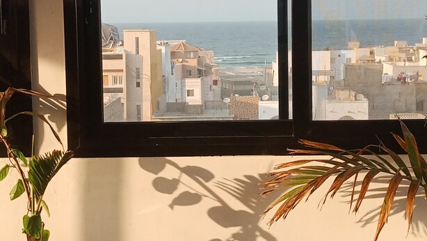 A view from a window overlooking a coastal cityscape with buildings and the sea. - Residence Hotel Kakatar (Dakar)