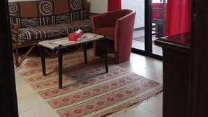 A living room with a sofa, a coffee table, a red armchair, a patterned rug, and a painting on the wall. - Residence Hotel Kakatar (Dakar)