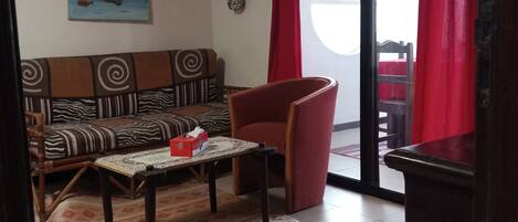 Una sala de estar con un sofá, una mesa de centro, un sillón rojo, un tapete estampado y un cuadro en la pared.