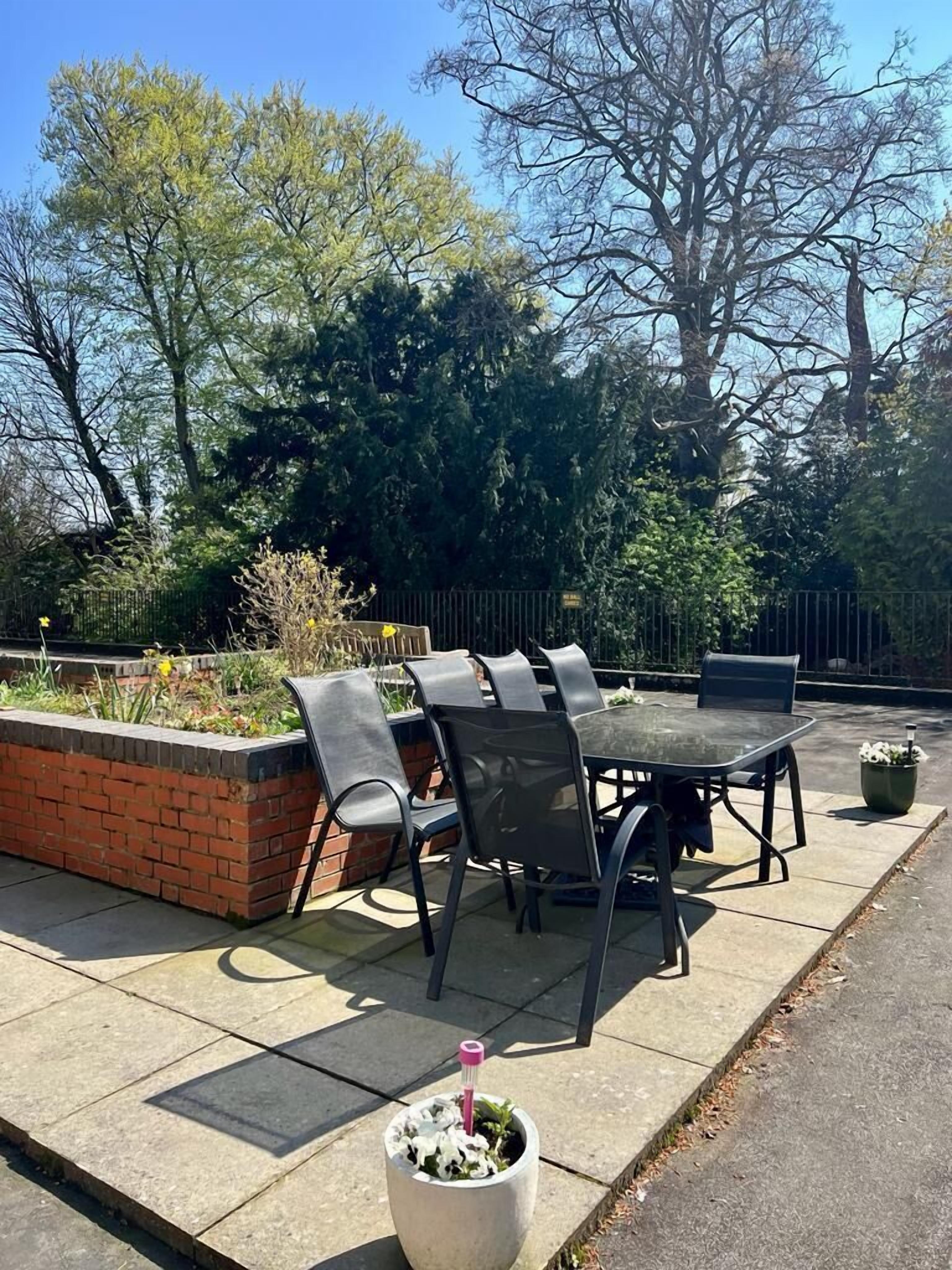 An outdoor patio with a table and chairs, surrounded by a brick planter and a metal fence.