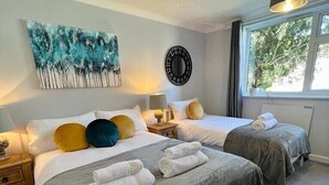 A hotel room with two beds, a painting on the wall, a round mirror, and a window with a view of trees. - Sunny 2-Bedroom flat in Hoddesdon (Hoddesdon)