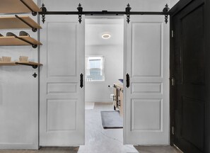 Un couloir avec une porte noire sur la droite, une porte blanche sur la gauche et une fenêtre donnant sur l’extérieur.