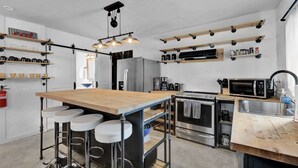 Una cocina moderna con una isla central, taburetes de bar, un refrigerador, un microondas y varios estantes con utensilios de cocina.