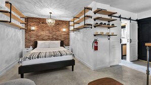 Un dormitorio moderno con pared de ladrillo, cama con ropa de cama estampada, estanterías de madera y una araña.