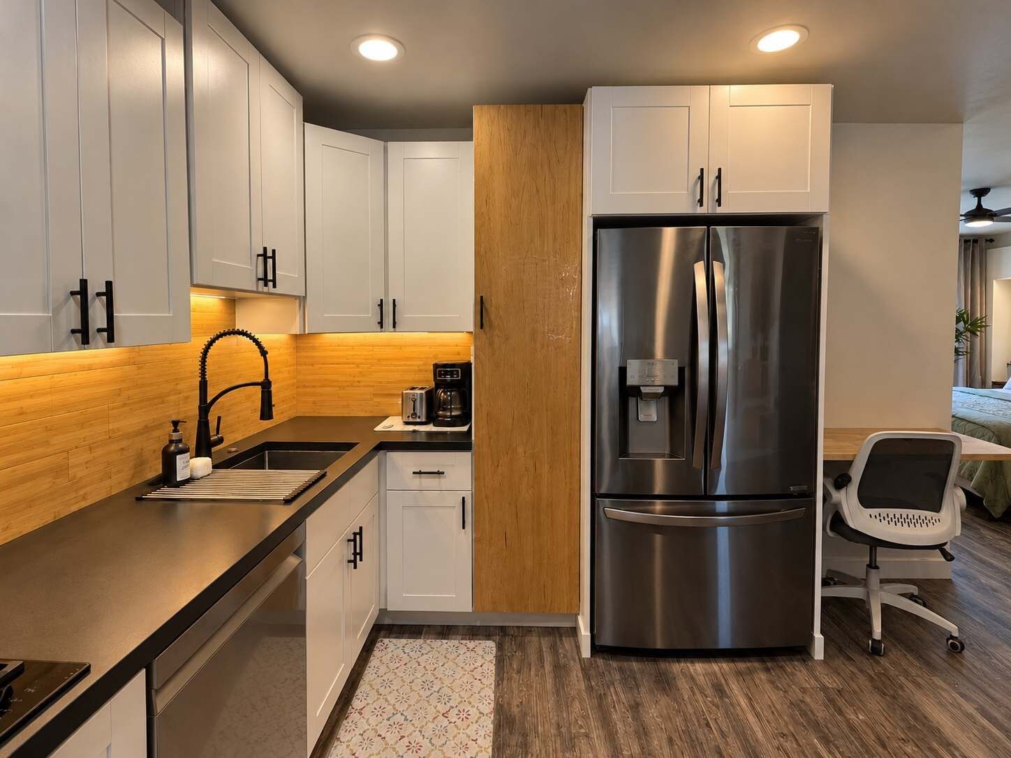 Una cocina moderna con armarios blancos, un refrigerador de acero inoxidable, una cafetera y un lavamanos pequeño.