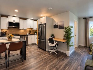 A modern kitchen with white cabinets, a stainless steel refrigerator, and a dining area with two chairs. - Double Queen Studio*FullKitchen*75"TV*W/D*Rainfall (El Centro)