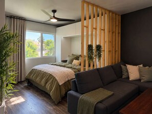 A modern bedroom with a bed, a sofa, a ceiling fan, and a window with curtains. - Double Queen Studio*FullKitchen*75"TV*W/D*Rainfall (El Centro)