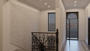 Un pasillo con paredes decoradas, una escalera con barandillas ornamentales y ventanas decorativas.