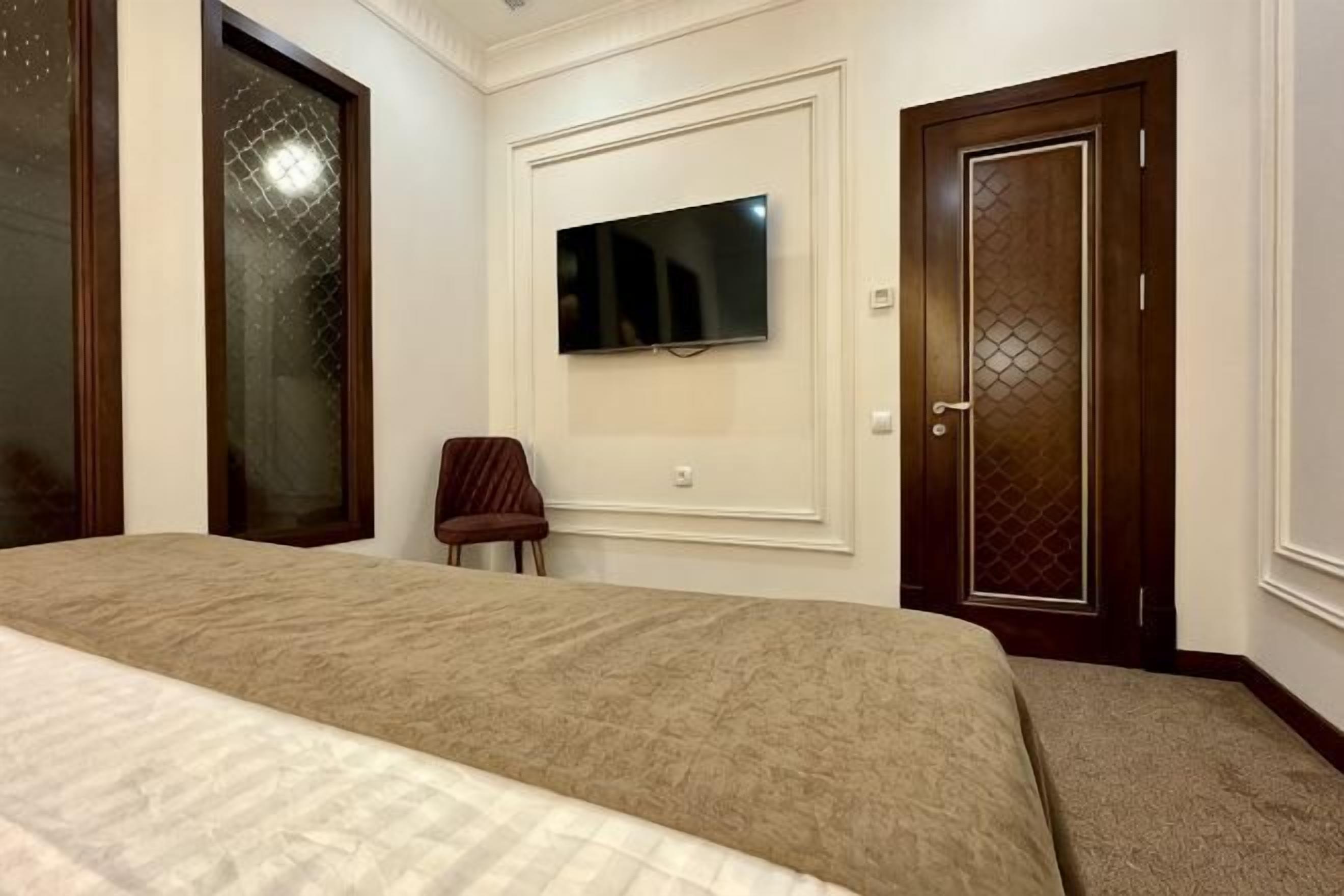 Een slaapkamer met een bed, een aan de muur bevestigde televisie en een deur met decoratieve panelen.