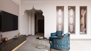 Un salón moderno con un televisor de pantalla plana, un sofá azul, una pequeña mesa redonda y objetos decorativos sobre un aparador.