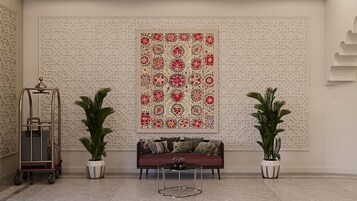 A lobby with a patterned wall, a sofa, two potted plants, and a cart.