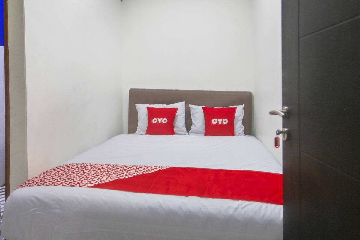 A small, neatly made bed with a white and red bedspread and two pillows with "OYO" branding.