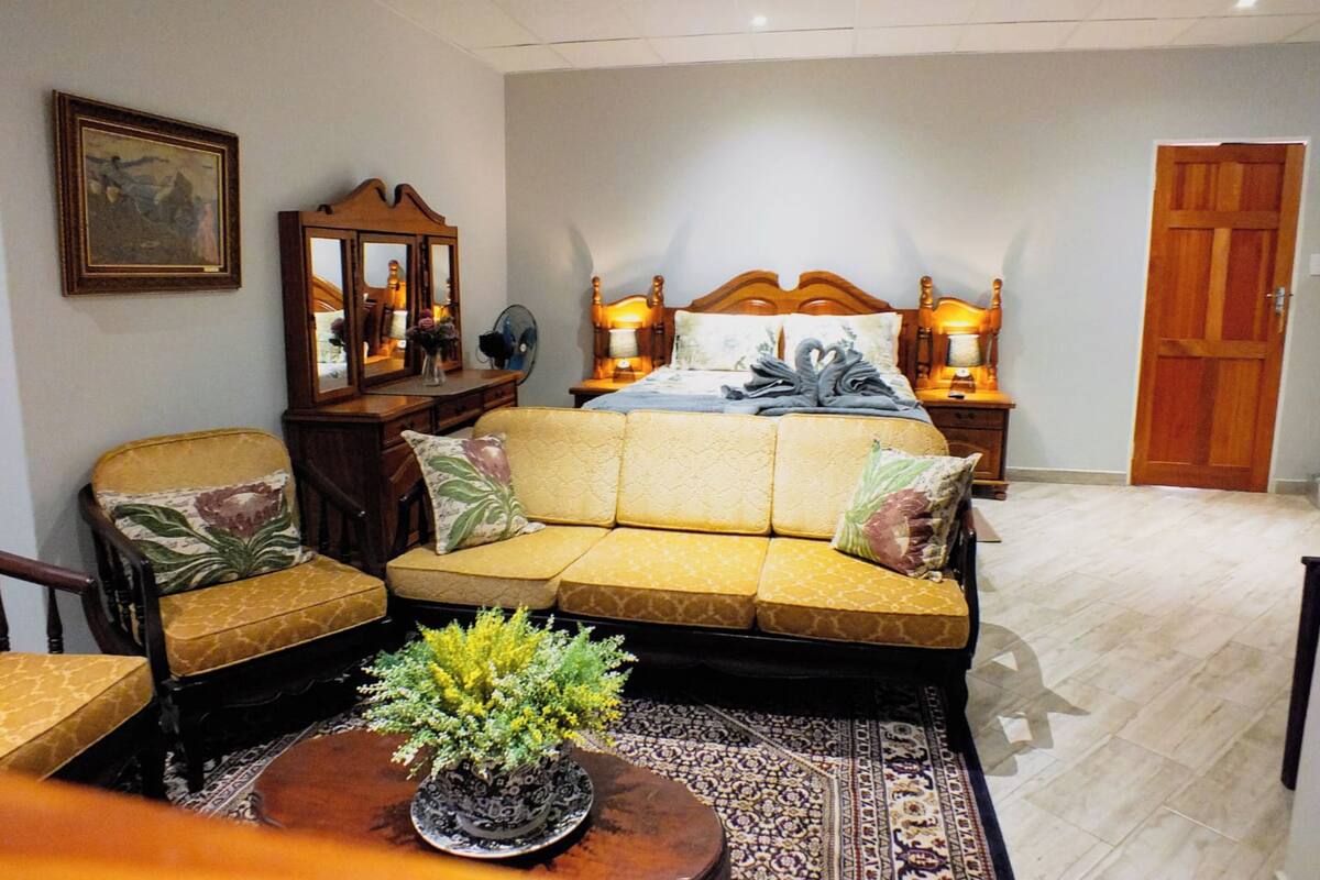 Un dormitorio con cama, mesitas de noche, cabecero de madera, espejo, silla y una pequeña mesa con una planta.