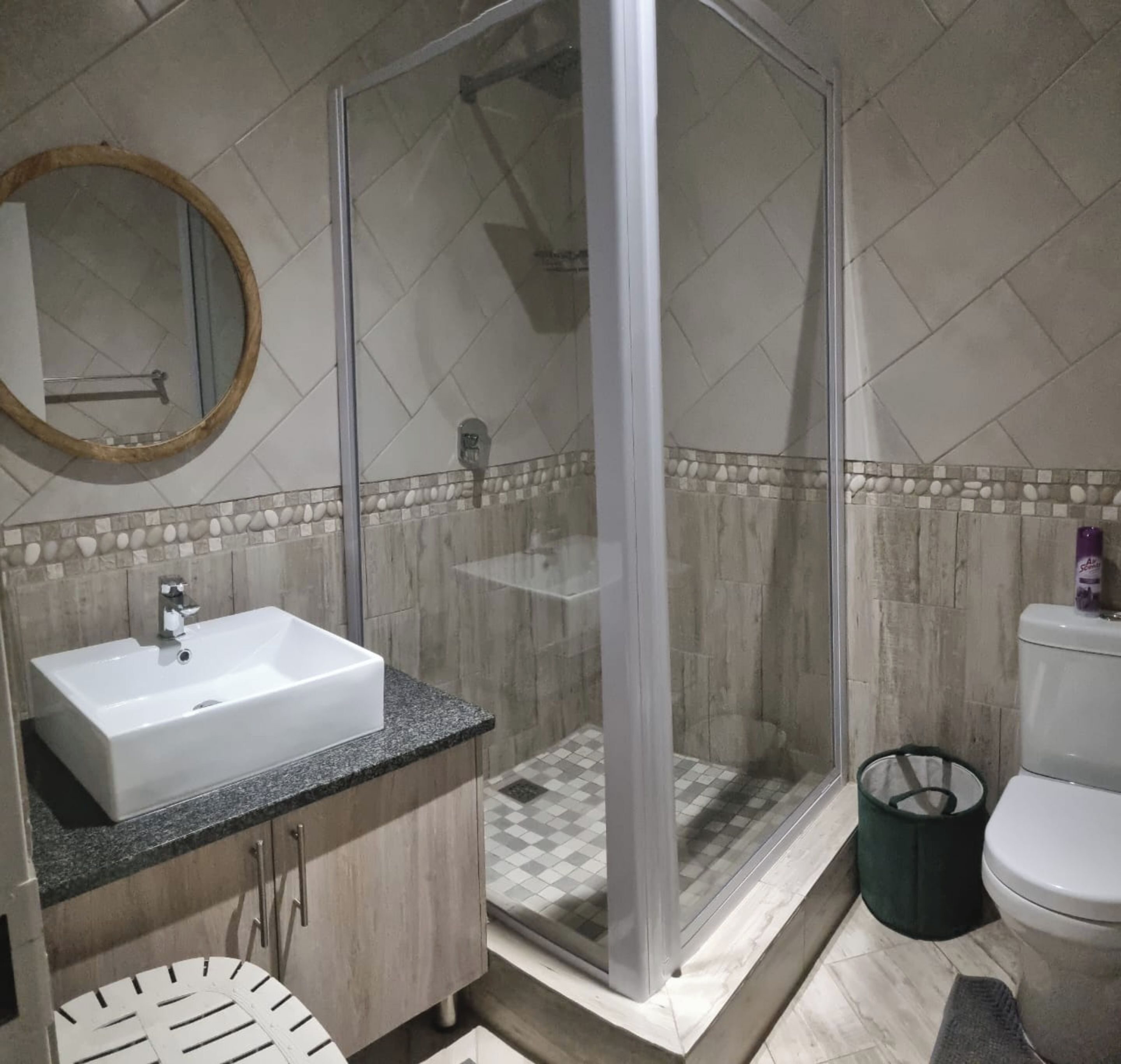 Een badkamer met een douche, wastafel, toilet en een spiegel.