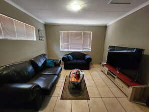 A living room with a black leather sofa, a black armchair, a coffee table, and a flat-screen TV on a wooden stand. - White Silo Accommodation (Thabazimbi)