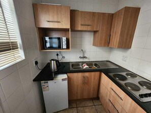 A compact kitchen with a microwave, stove, sink, and wooden cabinets. - White Silo Accommodation (Thabazimbi)