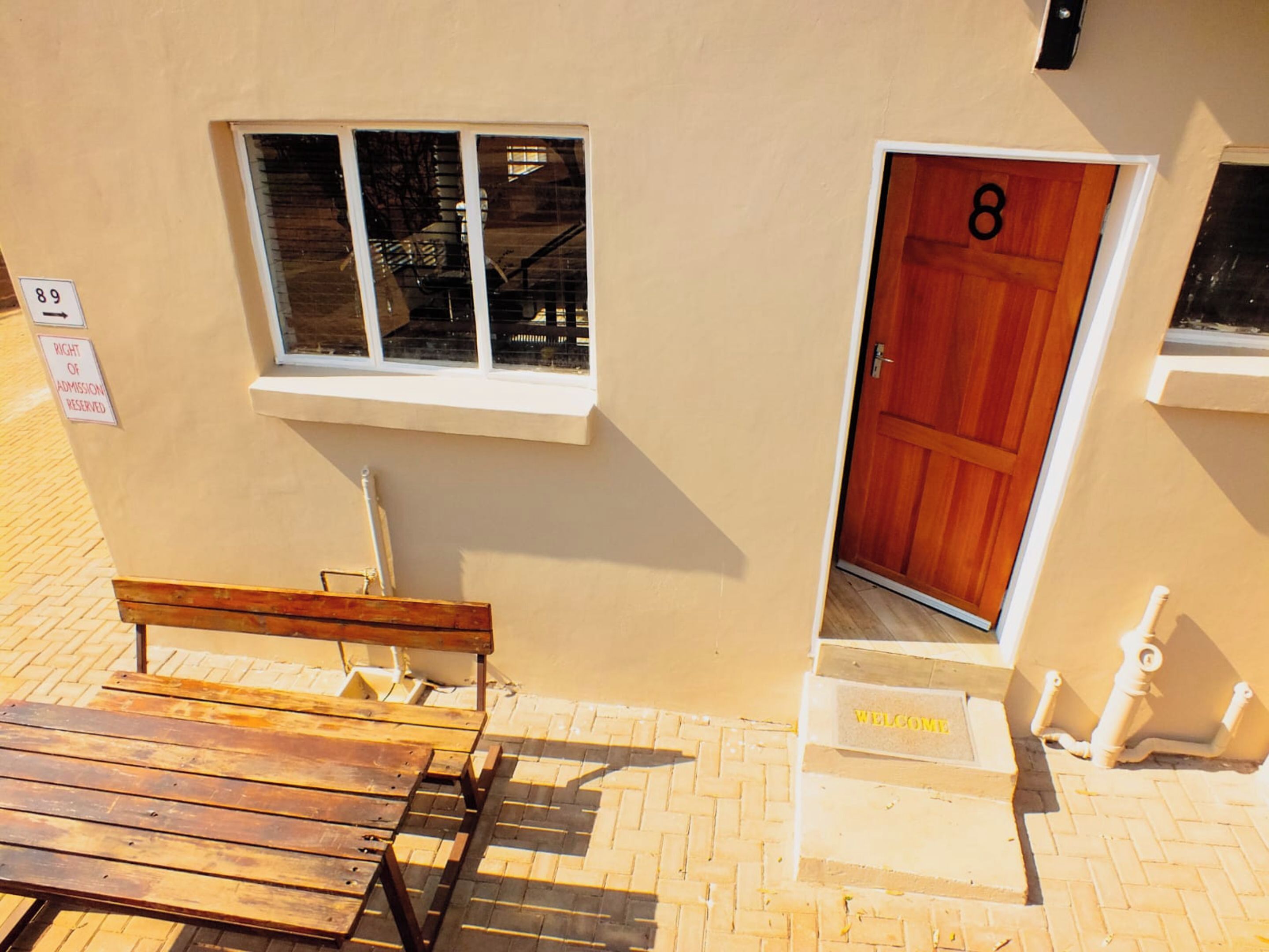 A building with a wooden door marked with the number 8, a window, a bench, and a welcome sign.