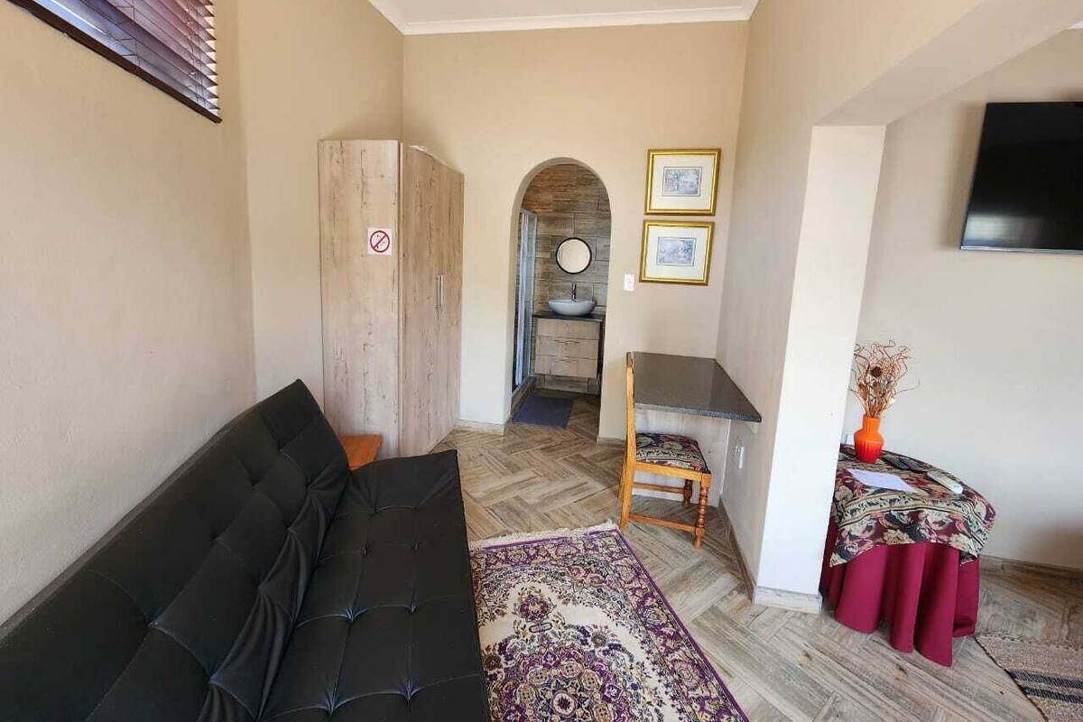 Una sala de estar con un sofá negro, un mueble de madera, una mesa de comedor con una silla y una mesita con un florero.