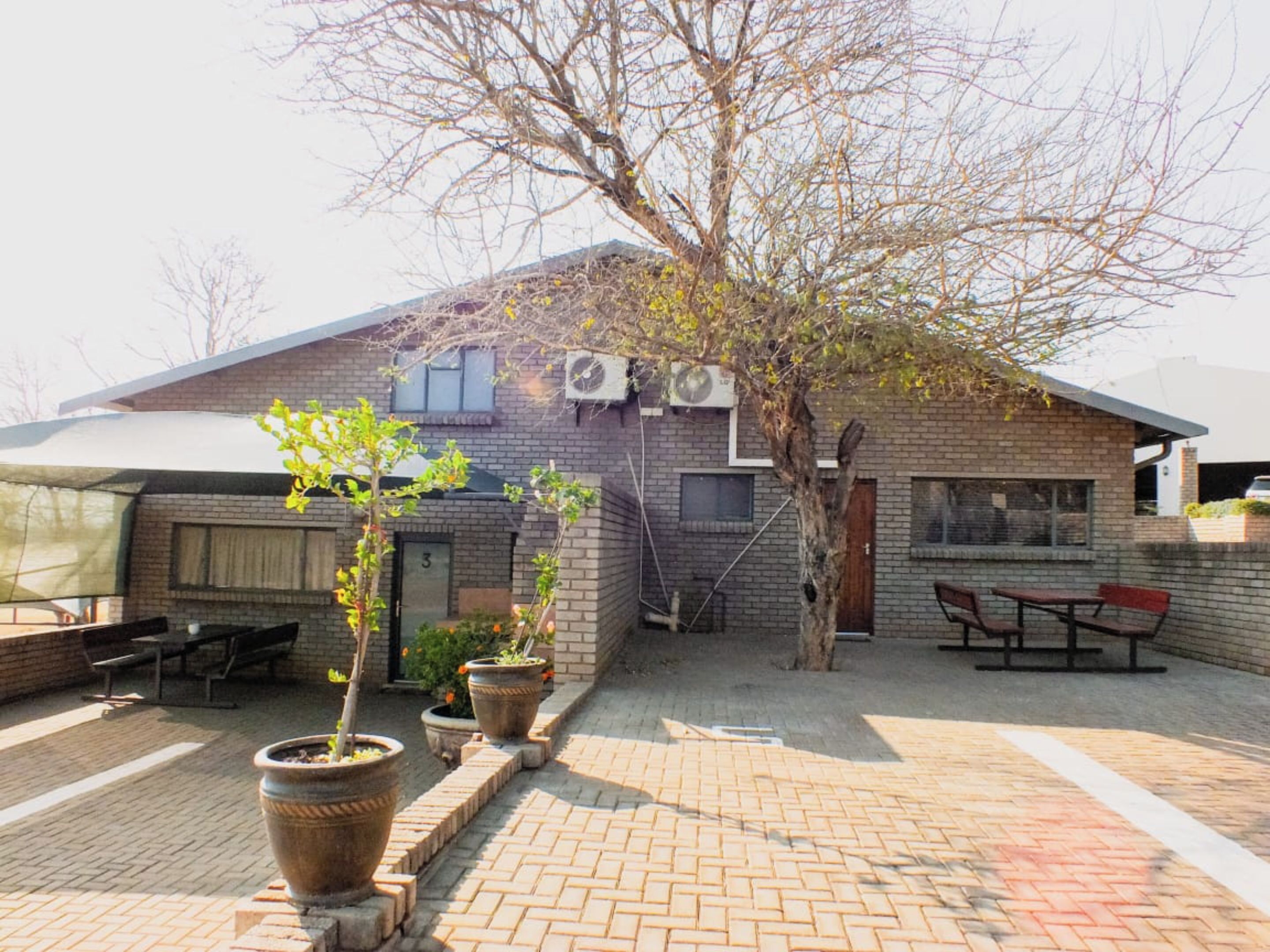 A brick building with a flat roof, outdoor seating area, and potted plants.