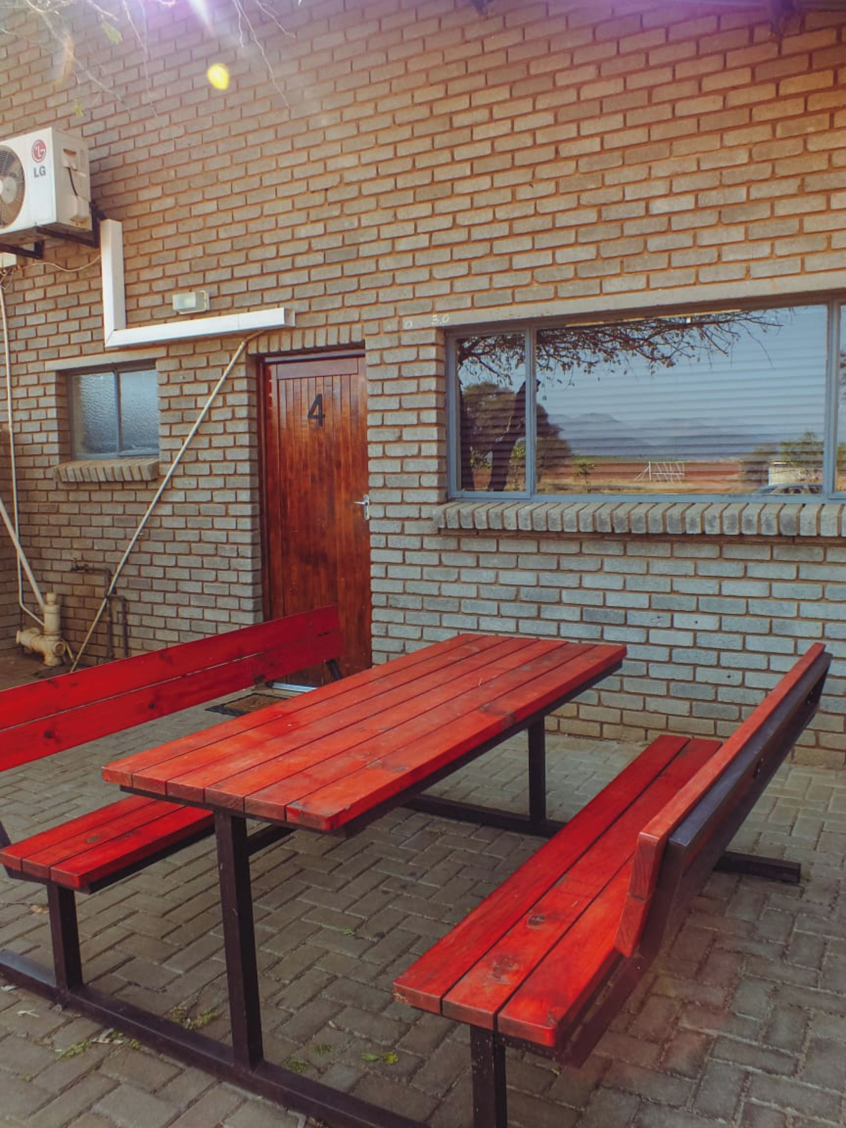 Ein Sitzbereich im Freien mit roten Bänken und Tischen, einer Ziegelwand und einem Fenster mit Blick auf die Landschaft.