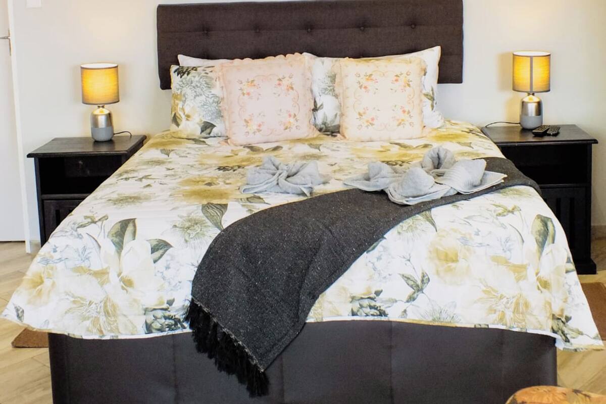 Una cama con una colcha estampada, dos lámparas de noche y un cabecero oscuro.