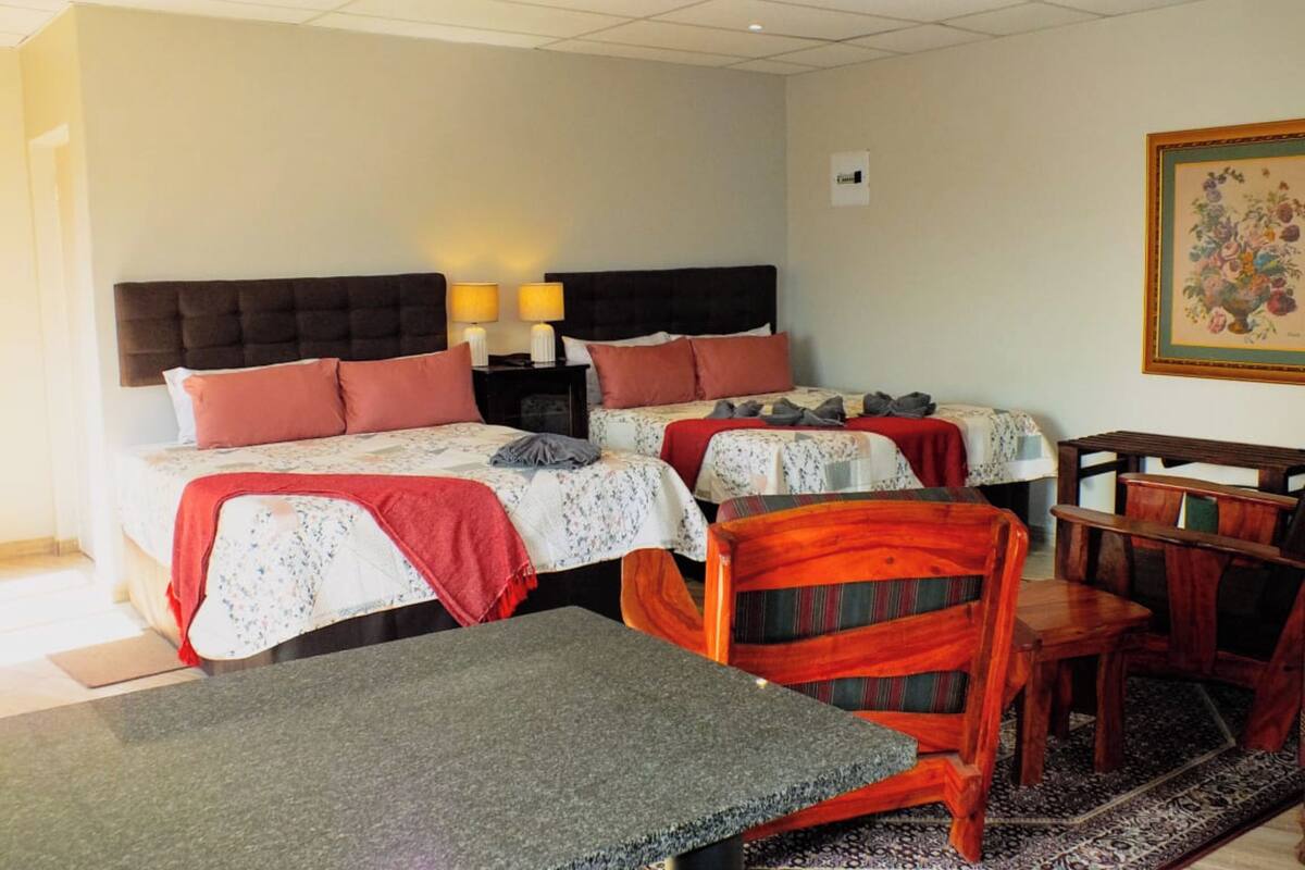 Habitación de hotel con dos camas, un escritorio, una silla y una mesita.