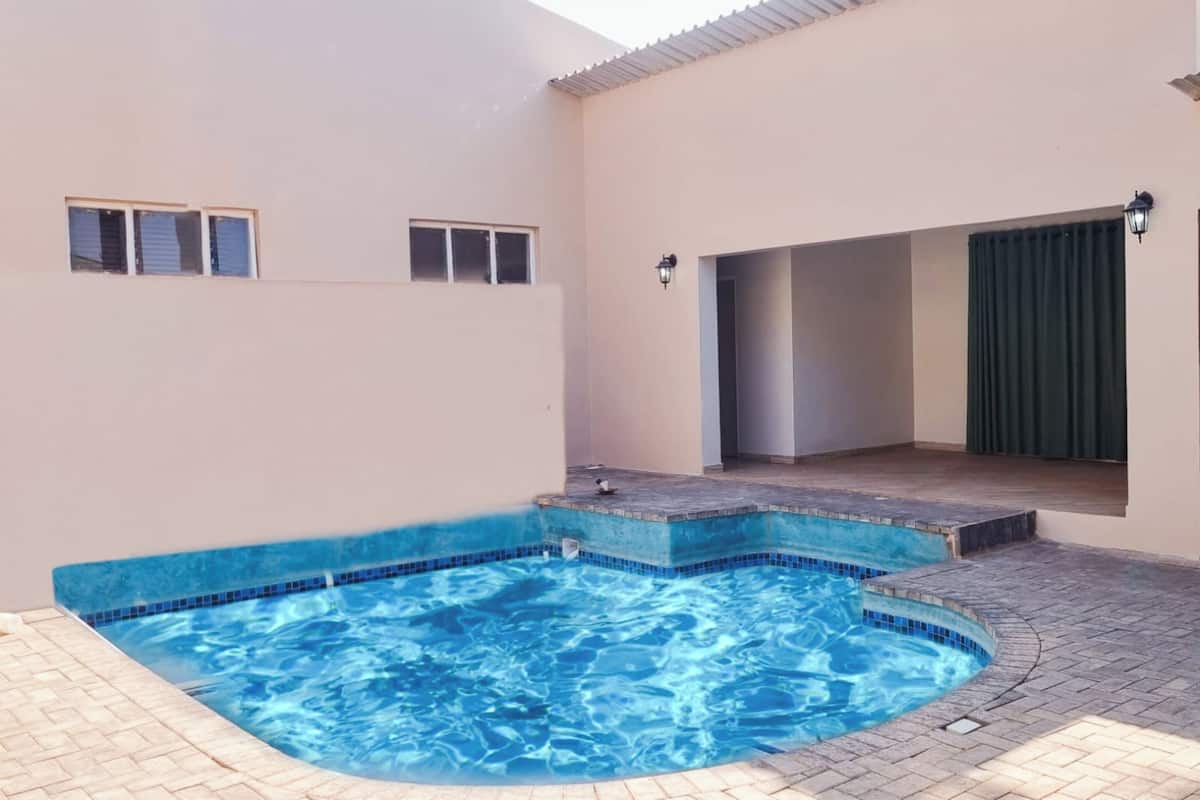 Una piscina con borde de azulejos, un patio techado y una puerta que da a un espacio interior.