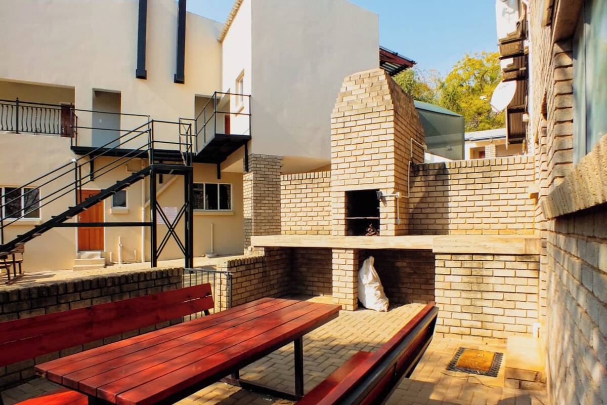 Un patio exterior con un horno de ladrillo, bancos de madera y una escalera que lleva a un nivel superior.