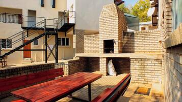 Un patio exterior con un horno de ladrillo, bancos de madera y una escalera que lleva a un nivel superior.