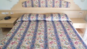 A bed with a floral-patterned bedspread and matching pillows, a wooden headboard, and a bedside table with a lamp and a telephone. - hotel CASABLANCA (Lazise)