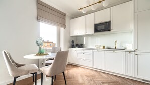 A modern kitchen with white cabinets, a microwave, and a dining area with two chairs and a table. - MARGI Daphne Apartment (Szczecin)