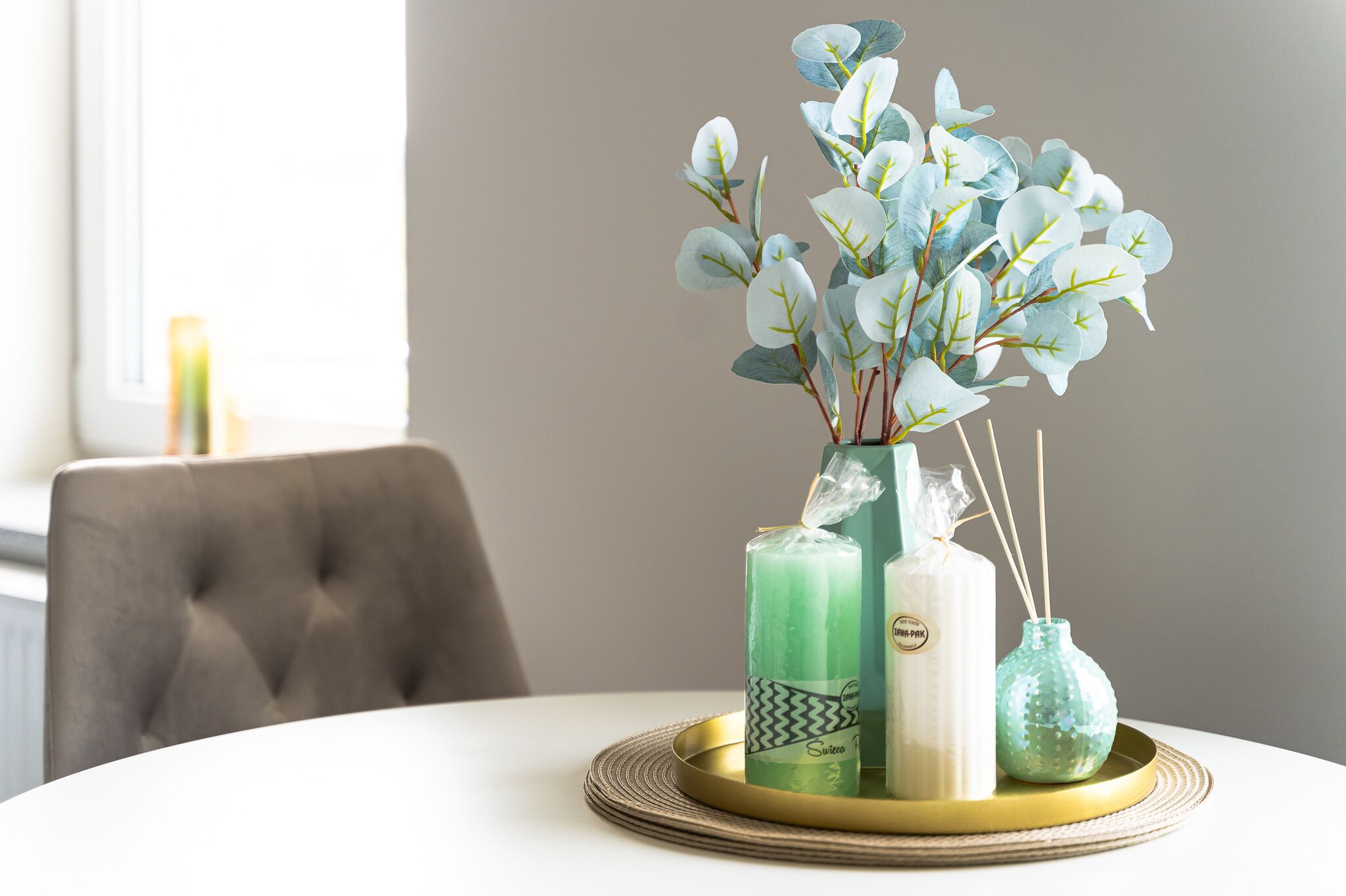 Una mesa con una decoración que incluye un florero con plantas artificiales, velas y un pequeño recipiente de vidrio.