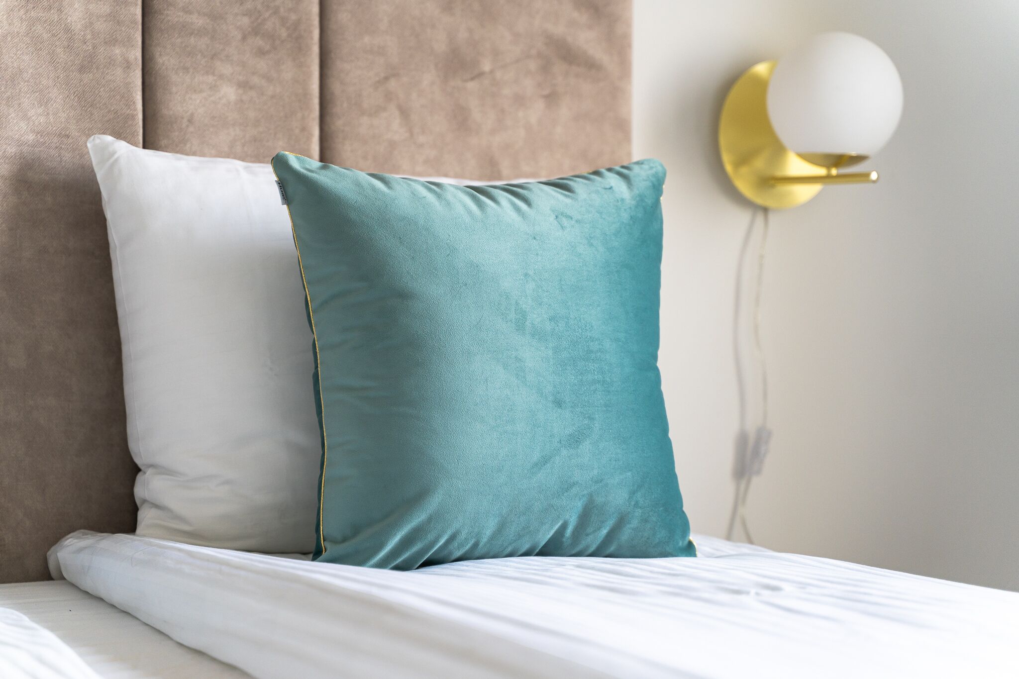 A bed with two pillows, one white and one teal, and a wall-mounted light fixture.
