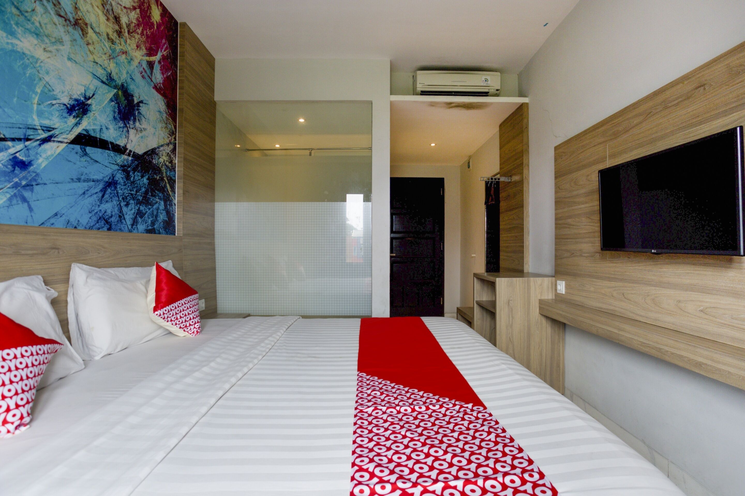Una habitación de hotel moderna con una cama grande, un televisor montado en la pared y un cuadro abstracto de gran tamaño sobre la cama.
