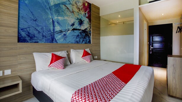 A modern hotel room with a large abstract painting on the wall, a neatly made bed with red and white pillows, and a red and white patterned throw. - Collection O Bekasi Timur Near Gedung Juang Formerly Regia Tambun (Cikarang)