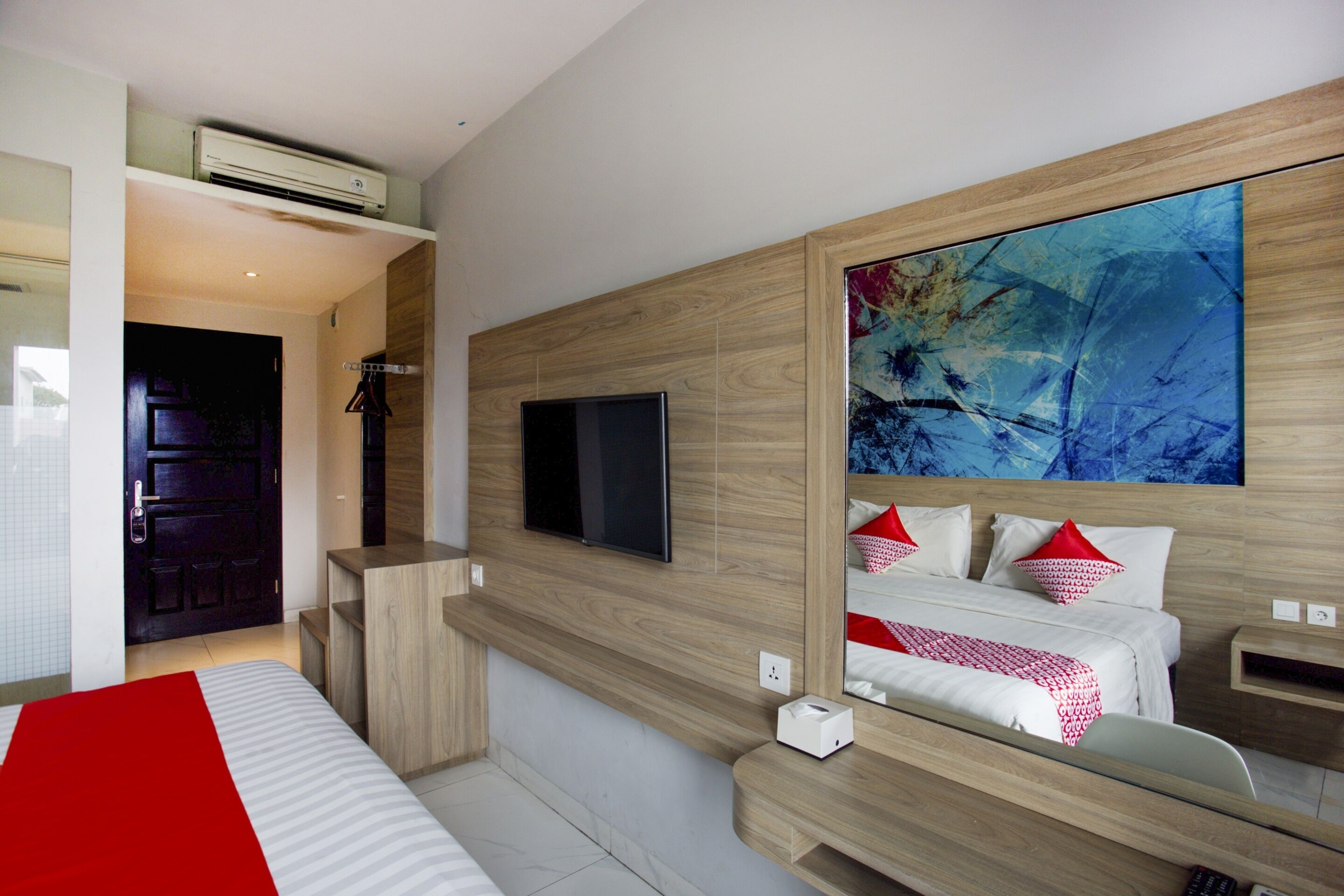 Une chambre d’hôtel moderne avec un grand lit, un téléviseur fixé au mur, une tête de lit en bois et un grand tableau abstrait.