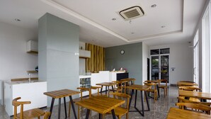 A modern dining area with wooden tables and chairs, a kitchen counter, and a clock on the wall. - Collection O Bekasi Timur Near Gedung Juang Formerly Regia Tambun (Cikarang)