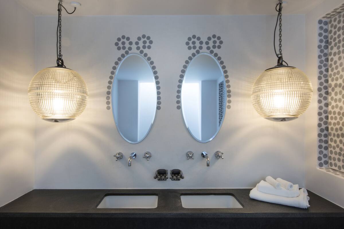 Uma casa de banho moderna com dois espelhos ovais, luzes pendentes e um porta-toalhas.