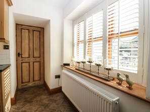 Eine Küche mit Holztür, weißen Fliesenwänden, einer Heizung und einem Fenster mit weißen Läden.
