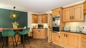 Eine kleine Küche mit Holzausstattung, einem eingebauten Backofen und einer Essecke mit grünen Stühlen.