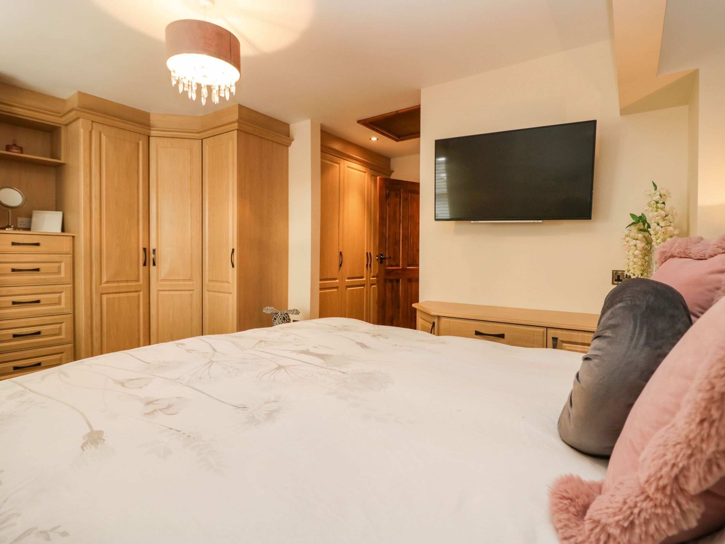 Une chambre à coucher avec un grand lit, une armoire en bois, un téléviseur à écran plat et un lustre.