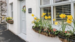 Ein weißes Cottage mit einem Schild, auf dem "Anvil Cottage" steht, eine Steinmauer und Blumenkästen mit Narzissen und anderen Blumen.