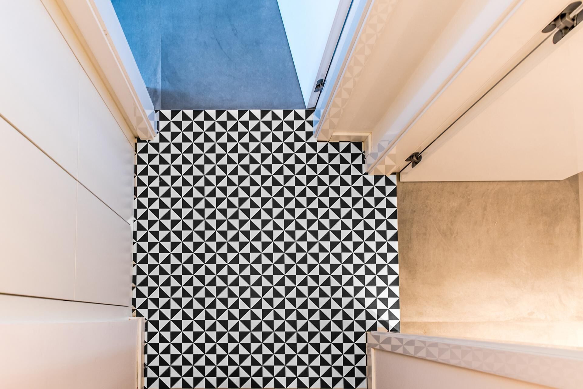 Una esquina de una habitación con un patrón geométrico blanco y negro en el suelo, paredes blancas y techo color beige.