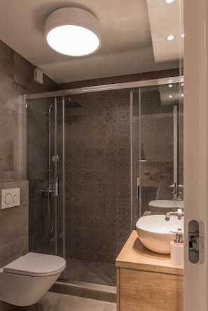 Un baño moderno con ducha de vidrio, inodoro y tocador con lavamanos.