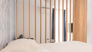 A hotel room with a bed, a small table, and a chair. There is a wooden partition with vertical slats, a wall with a textured pattern, and a ceiling light. - Deluxe, Charming and Cozy Bcadria Apartment A2 (Split)