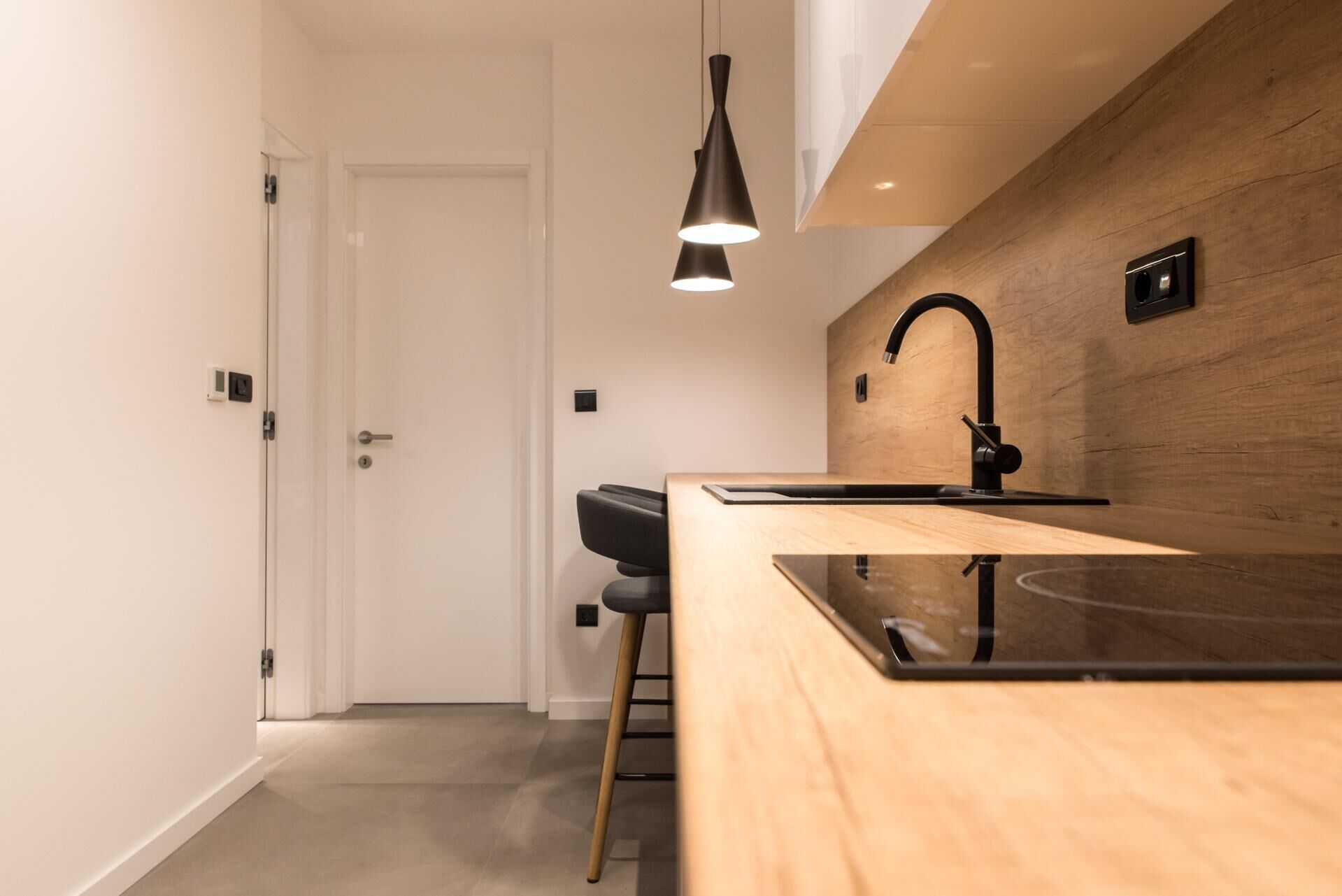 A modern kitchen with a wooden countertop, black faucet, and pendant lighting.