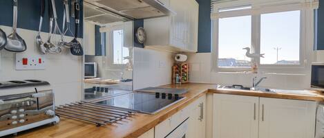 A modern kitchen with white cabinets, a wooden countertop, a built-in oven, and a window with blinds.