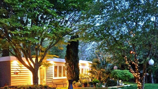 A well-maintained garden with a variety of trees and shrubs, a decorative metal planter, and a pathway leading to a building with warm lighting. - 1 Bed Cottage-museum View-garden-free Parking (Weybridge)